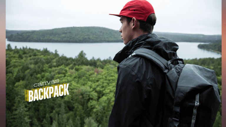 A solo traveler traveling with his canvas backpack on his shoulder and watching a lake